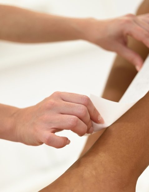 Woman having hair removal procedure on leg applying wax strip