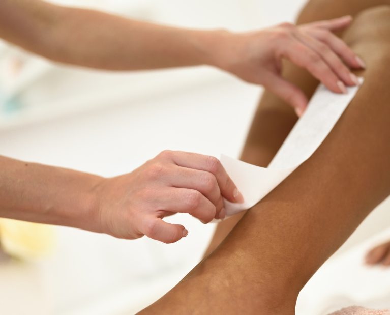 Woman having hair removal procedure on leg applying wax strip
